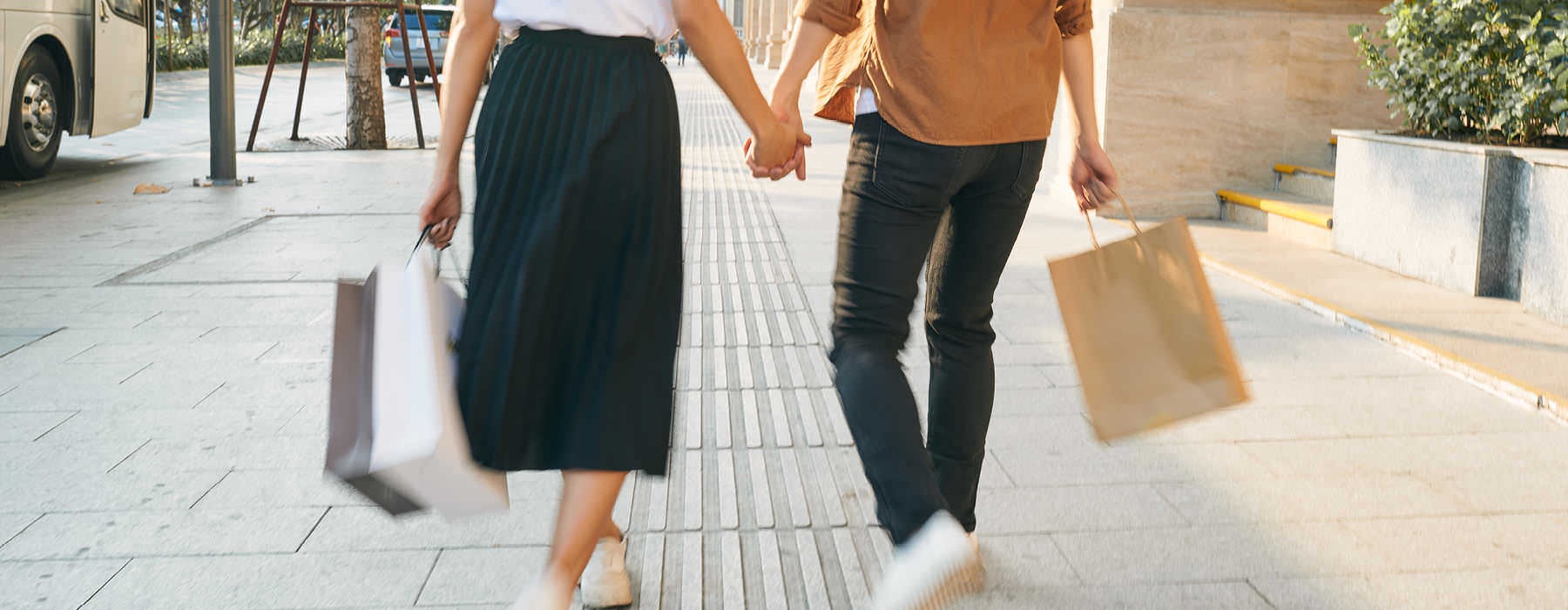 man and woman hold hands and walk down the street with shopping bags